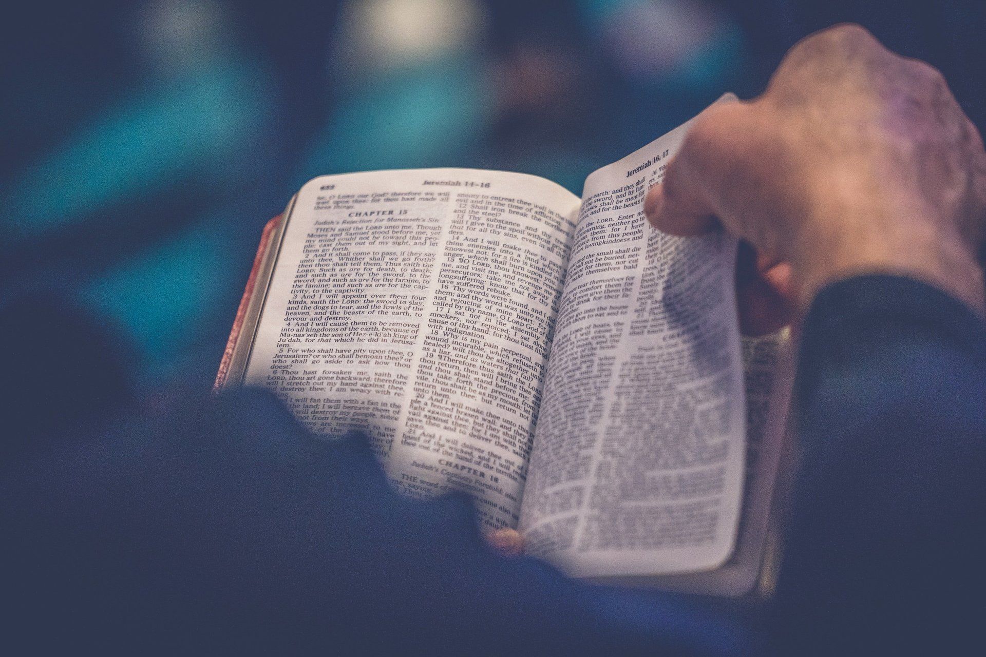 Person's hands holding open book, possibly a Bible, reading indoors.